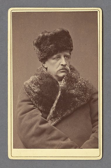 Svartvitt fotografi av man med mustasch, iklädd vinterrock med pälskrage och pälsmössa.
